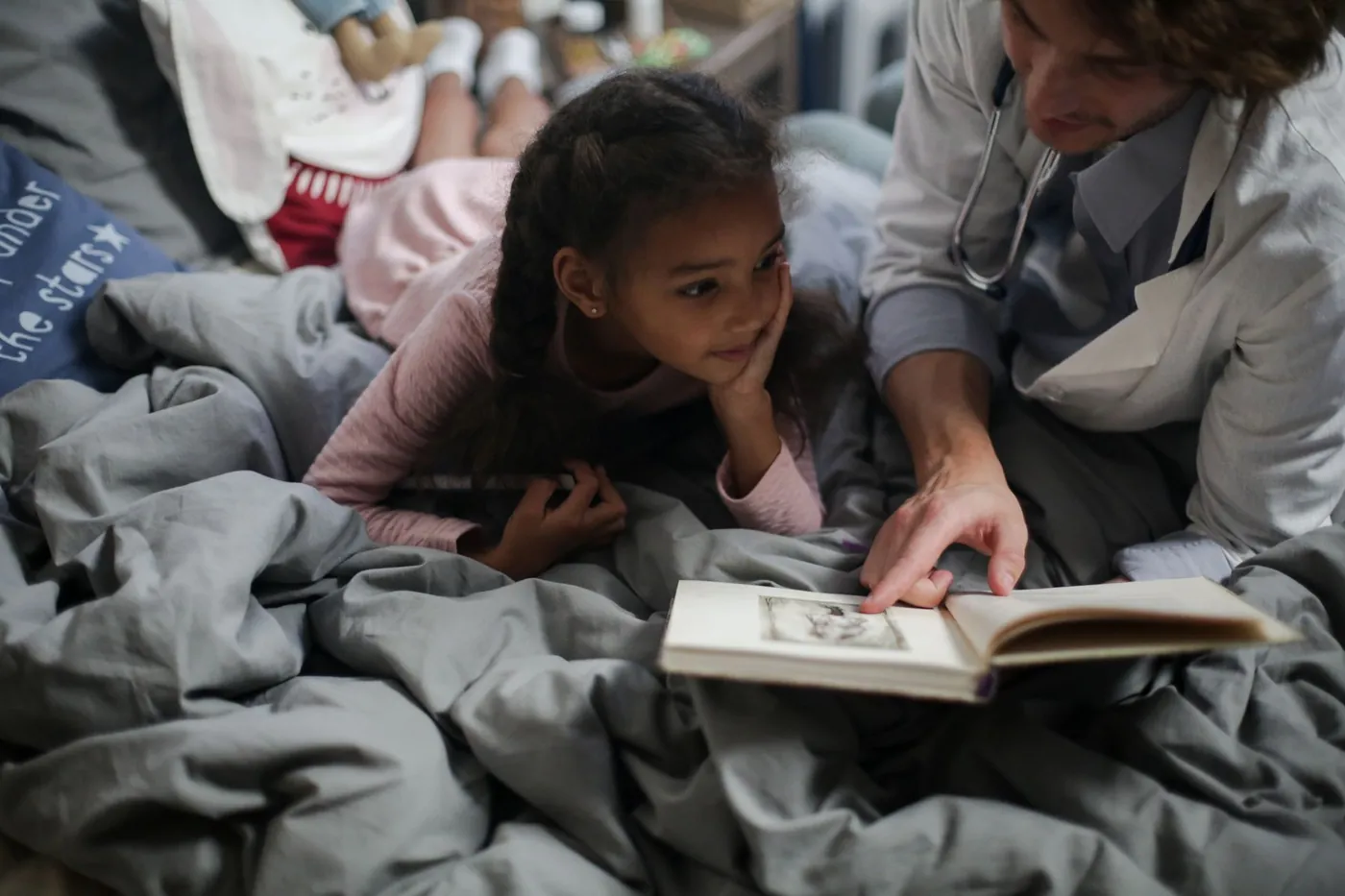 A clinician reads a book with a young girl at home