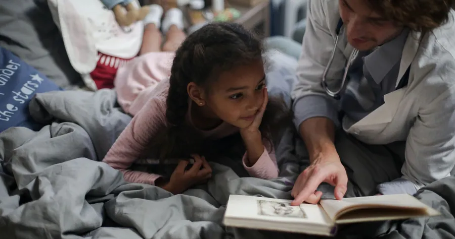A clinician reads with a young girl at home